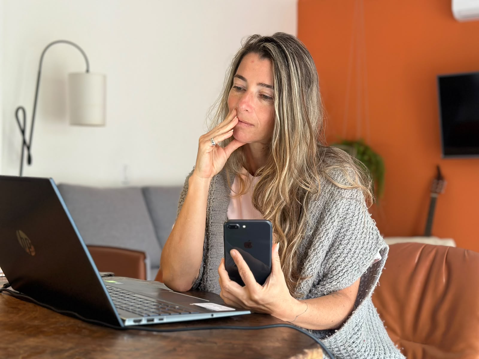 Ana Tahan pensativa, com a mão no rosto, olhando o celular na mesa de trabalho
